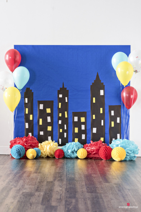 a party backdrop with a skyscraper scene and colorful balloons