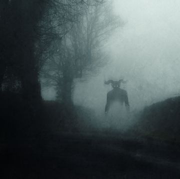 a supernatural demon. standing on a road. on a spooky foggy night in the countryside. with a grunge abstract edit.