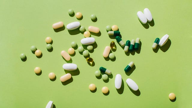 colorful pills and capsules on green background minimal medical concept flat lay, top view