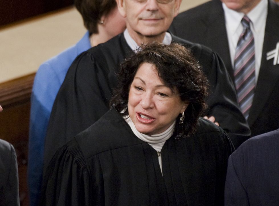 sonia sotomayor, wearing black judge robes, speaking to someone off camera in the middle of a crowded room