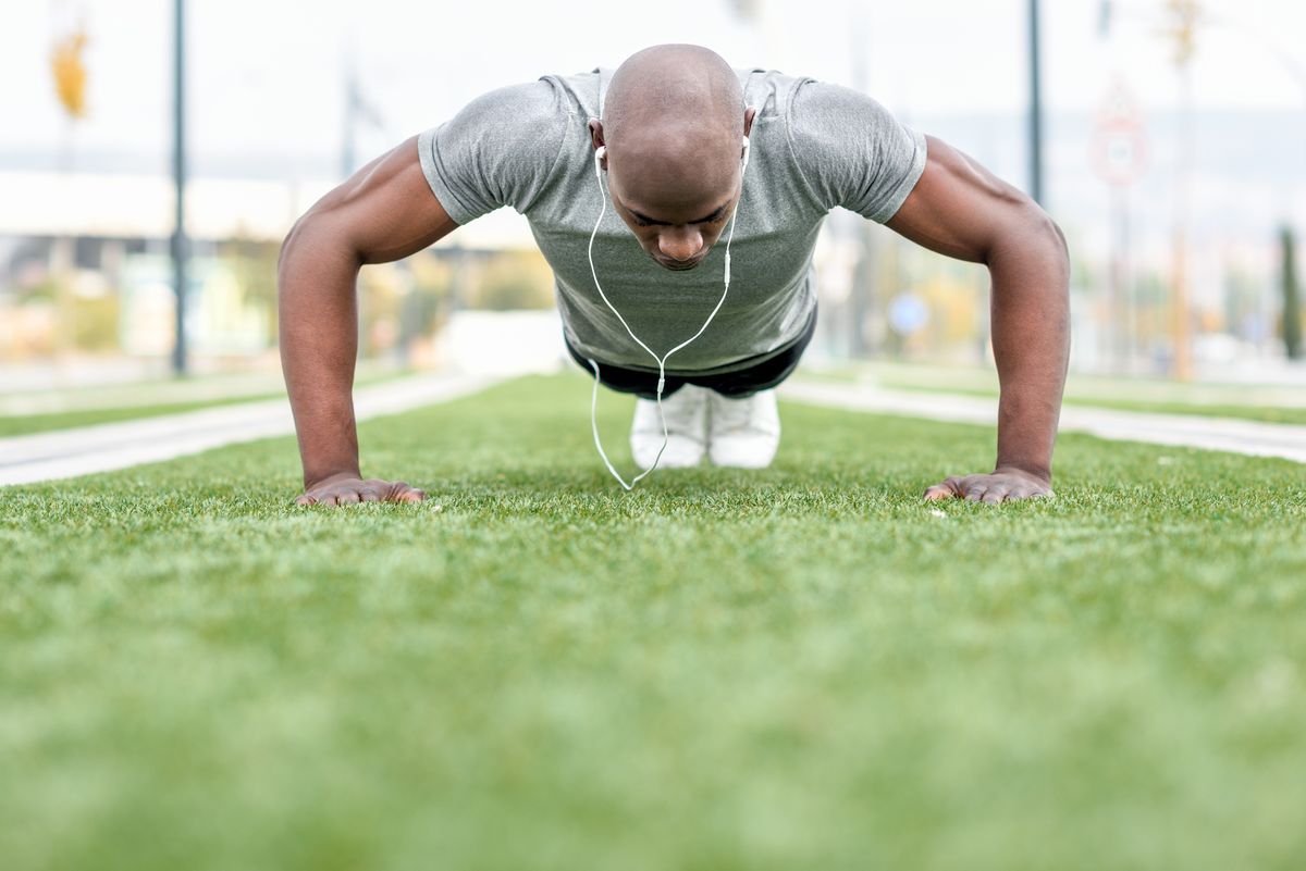 Surface Level View Of Man Doing Push-Ups On Grassy Field