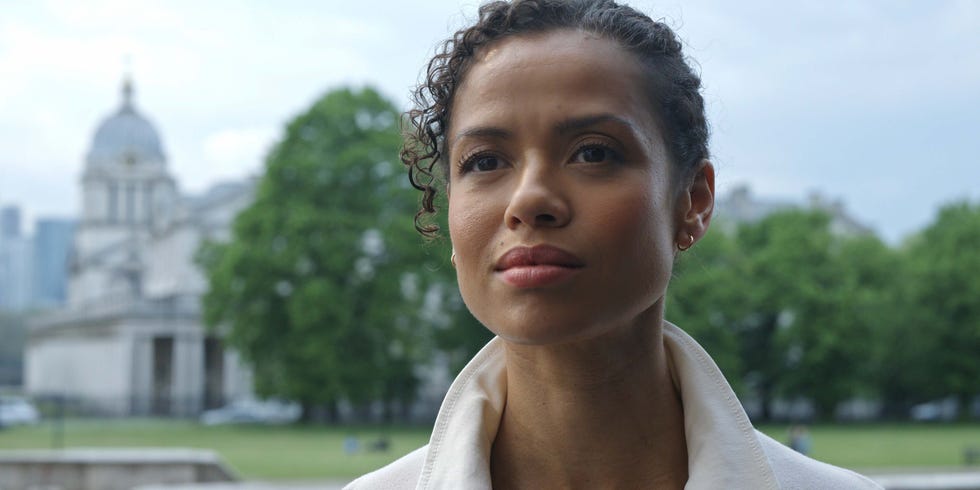 a person in a lightcolored jacket stands in front of a historic building and greenery