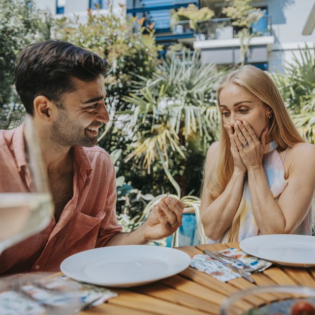 surprised woman looking at man with engagement ring at outdoor table