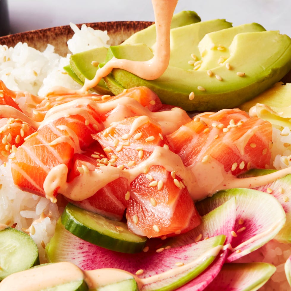sushi rice in a bowl topped with salmon, cucumber, watermelon radish, sliced avocado, and spicy mayo