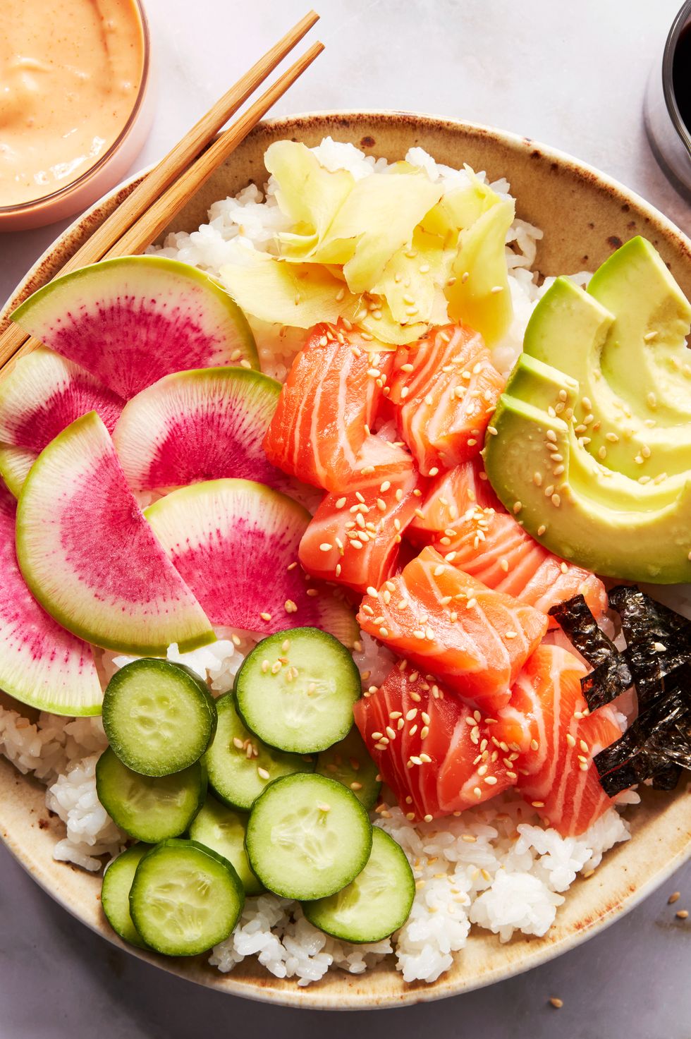 sushi rice in a bowl topped with salmon, cucumber, watermelon radish, sliced avocado, and spicy mayo