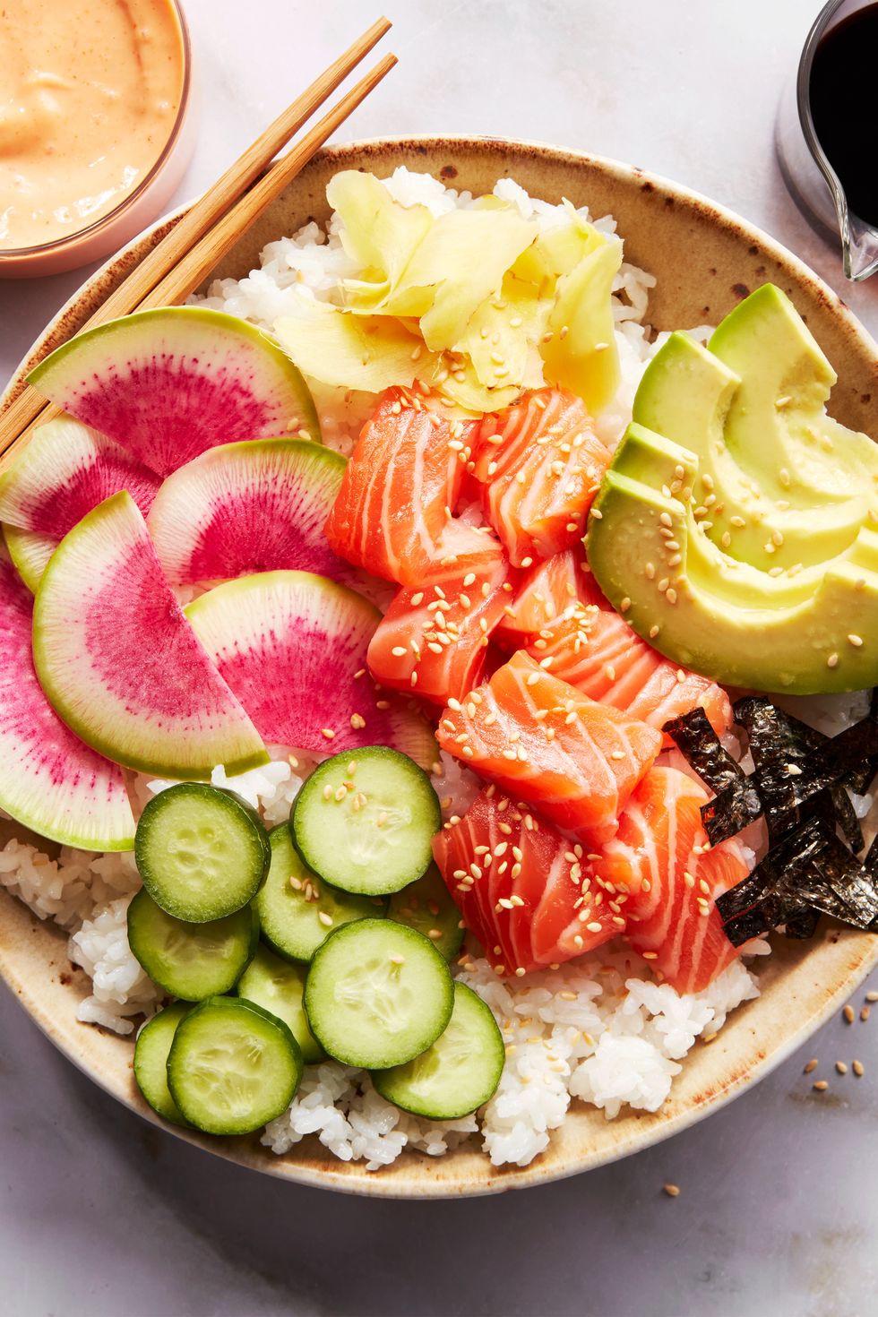 sushi rice in a bowl topped with salmon, cucumber, watermelon radish, sliced avocado, and spicy mayo
