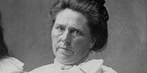 belle gunness sits for a photo with a blank expression on her face, she wears a white blouse and her hair is in a bun