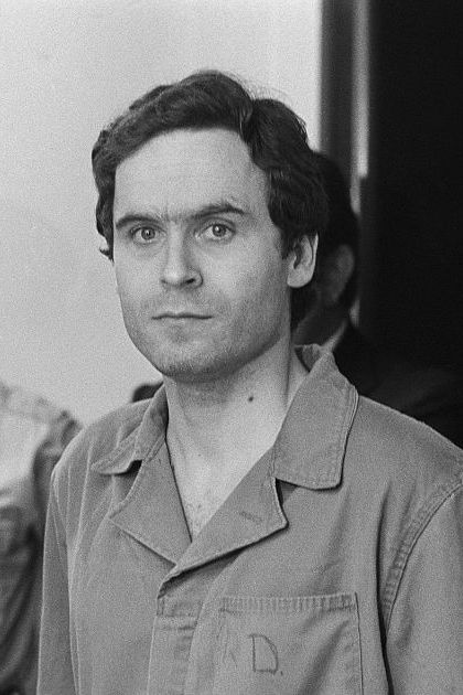 ted bundy surrounded by police and looking straight ahead as he walks into a court hearing