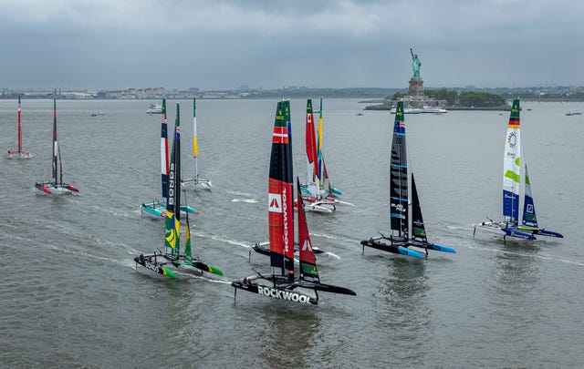 A equipe SailGP da Alemanha, apresentada pelo Deutsche Bank, comandada por Erik Heil, lidera a frota da SailGP passando pela Estátua da Liberdade durante a primeira corrida do Mubadala New York Sail Grand Prix, em Nova York, EUA. Sábado, 7 de junho de 2025. Evento do Campeonato Rolex SailGP, 6ª temporada de 2025. Foto: Samo Vidic para SailGP. Imagem do folheto fornecida pela SailGP.