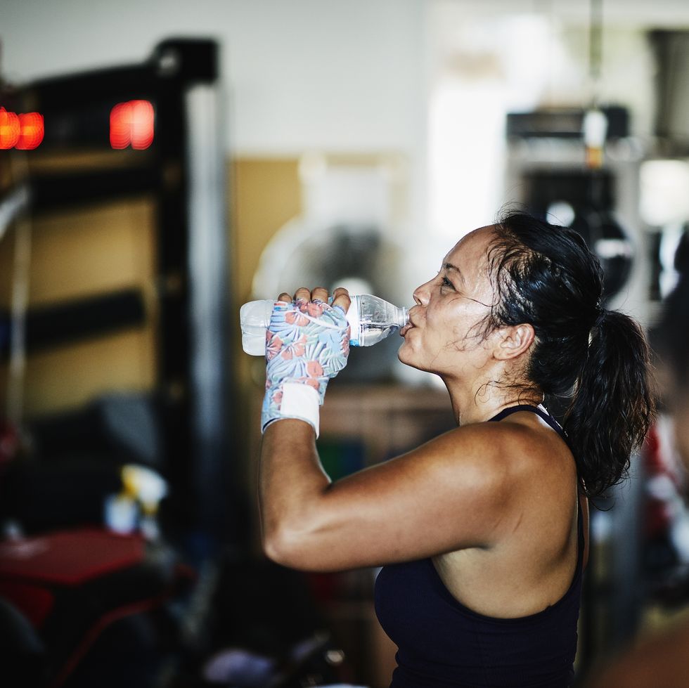 Sweating female boxer drinking water after workout in boxing gym
