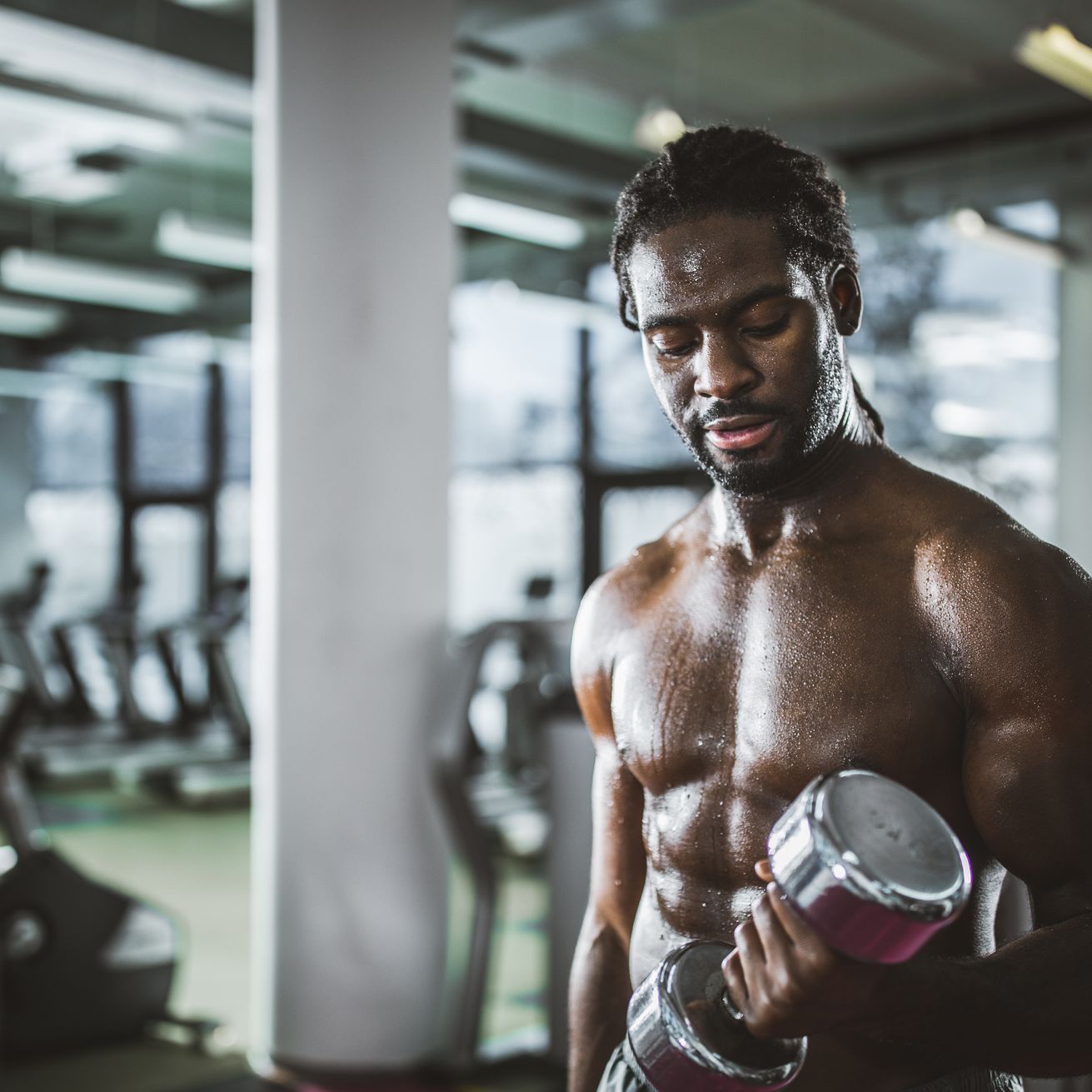 sweaty african american athlete exercising with dumbbell in a gym