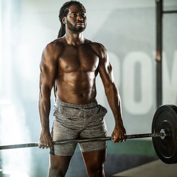 sweaty african american athletic man exercising with barbell in a gym