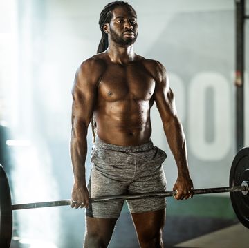 sweaty african american athletic man exercising with barbell in a gym