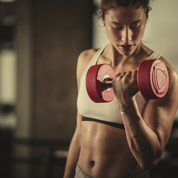 Sweaty athletic woman exercising with dumbbells in a health club.