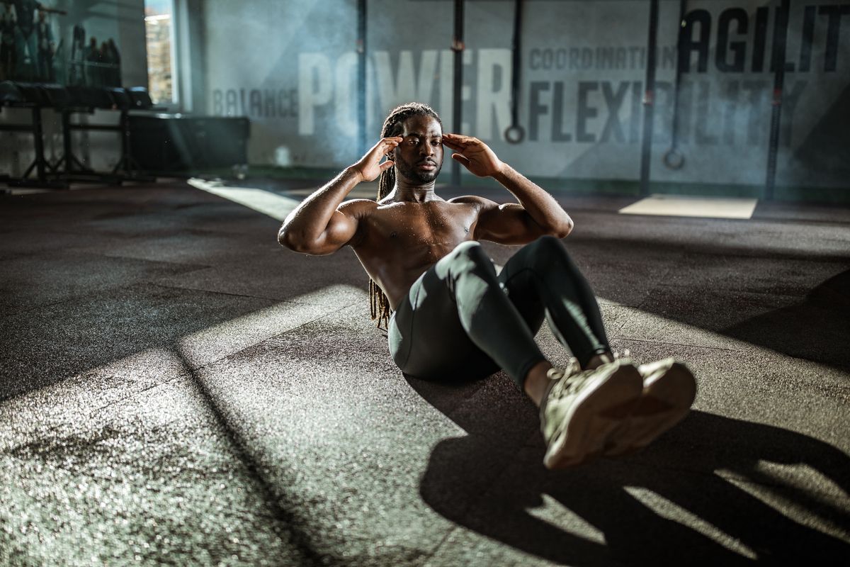 Sweaty black athlete doing sit-ups in a gym.
