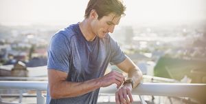 Sweaty male runner resting checking smart watch fitness tracker at sunny urban railing