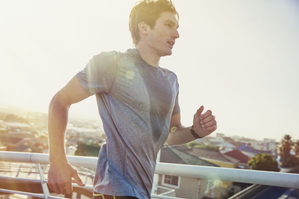 Sweaty male runner running on sunny urban footbridge at sunrise