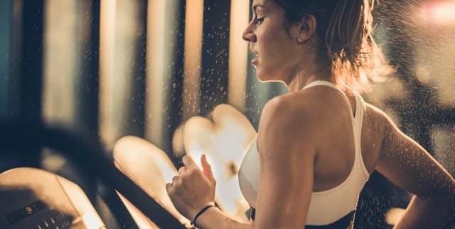 Sweaty woman running on treadmill during sports training in a gym.