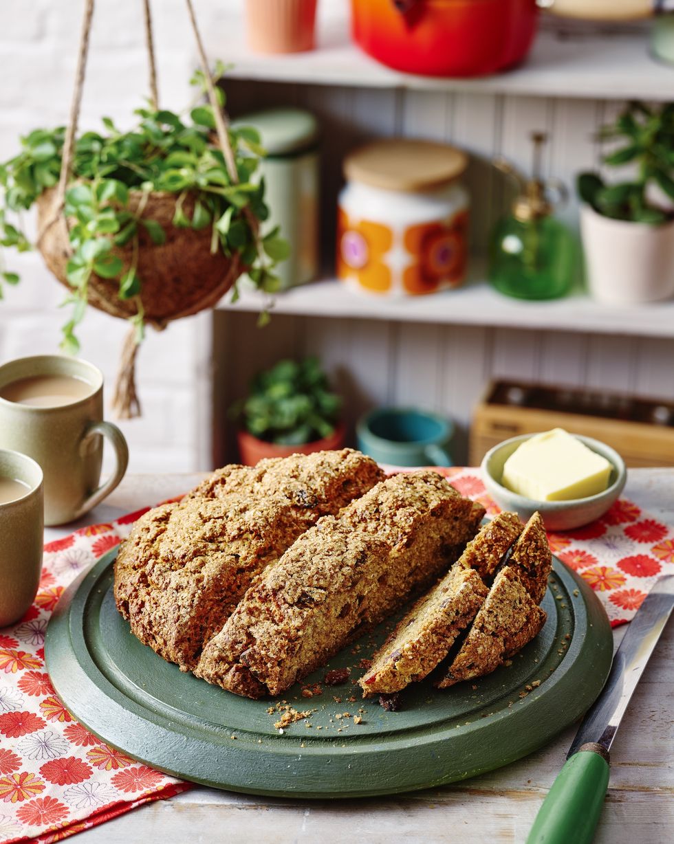 sliced soda bread on a wooden chopping board with a floral table cloth and house plant in the background