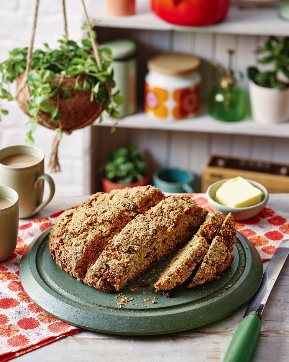 sliced soda bread on a wooden chopping board with a floral table cloth and house plant in the background