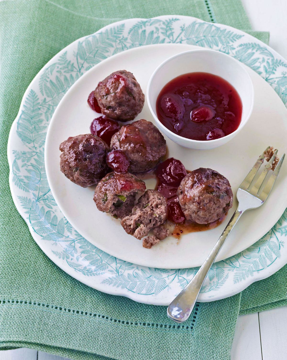 sweet and sour meatballs on a green and white plate with cranberry dipping sauce