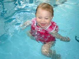 toddler swimming in a pool wearing a life vest and swim diaper