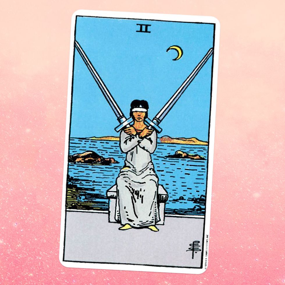 the tarot card the two of swords, showing a blindfolded person in a white robe holding two swords crossed in front of them
