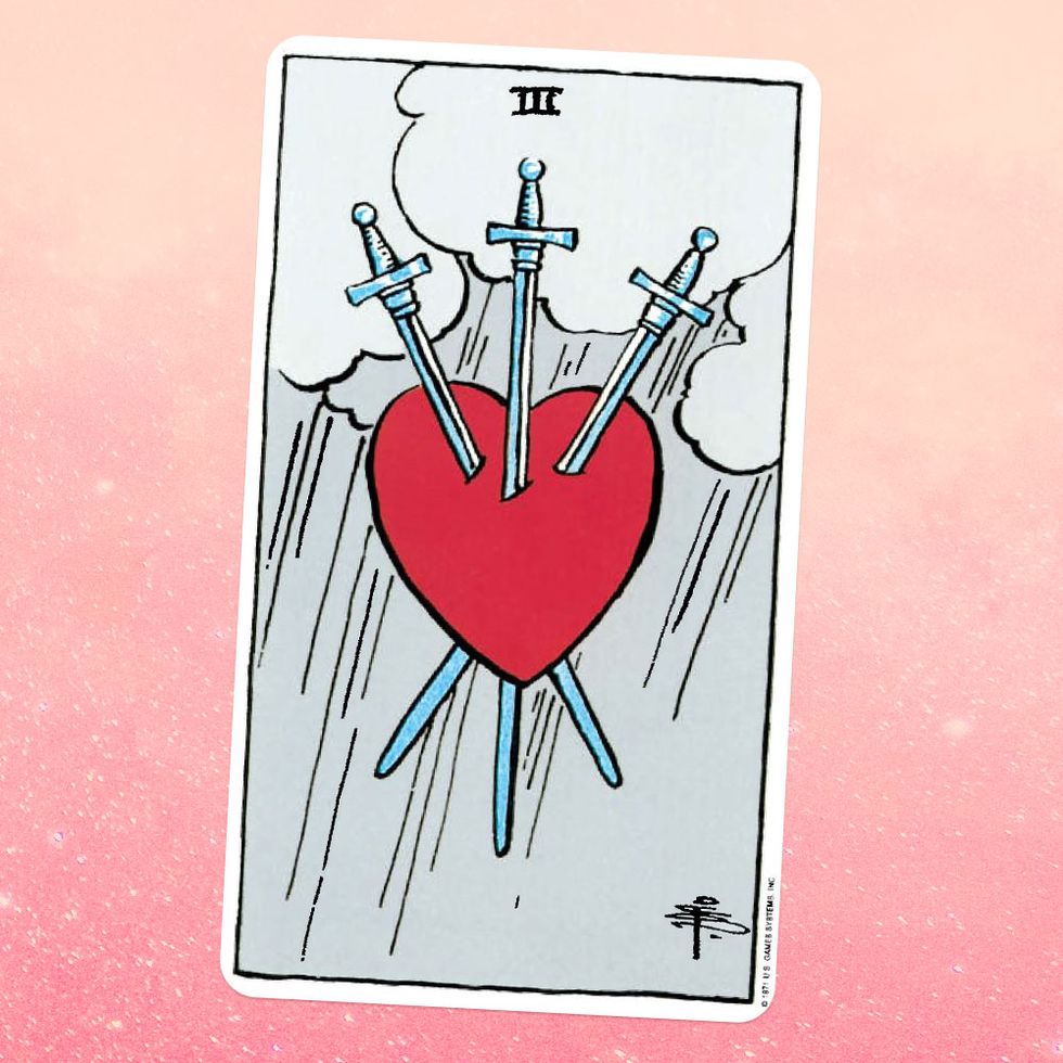 the tarot card the three of swords, showing a red heart stuck through with three swords, with a rainy sky behind it