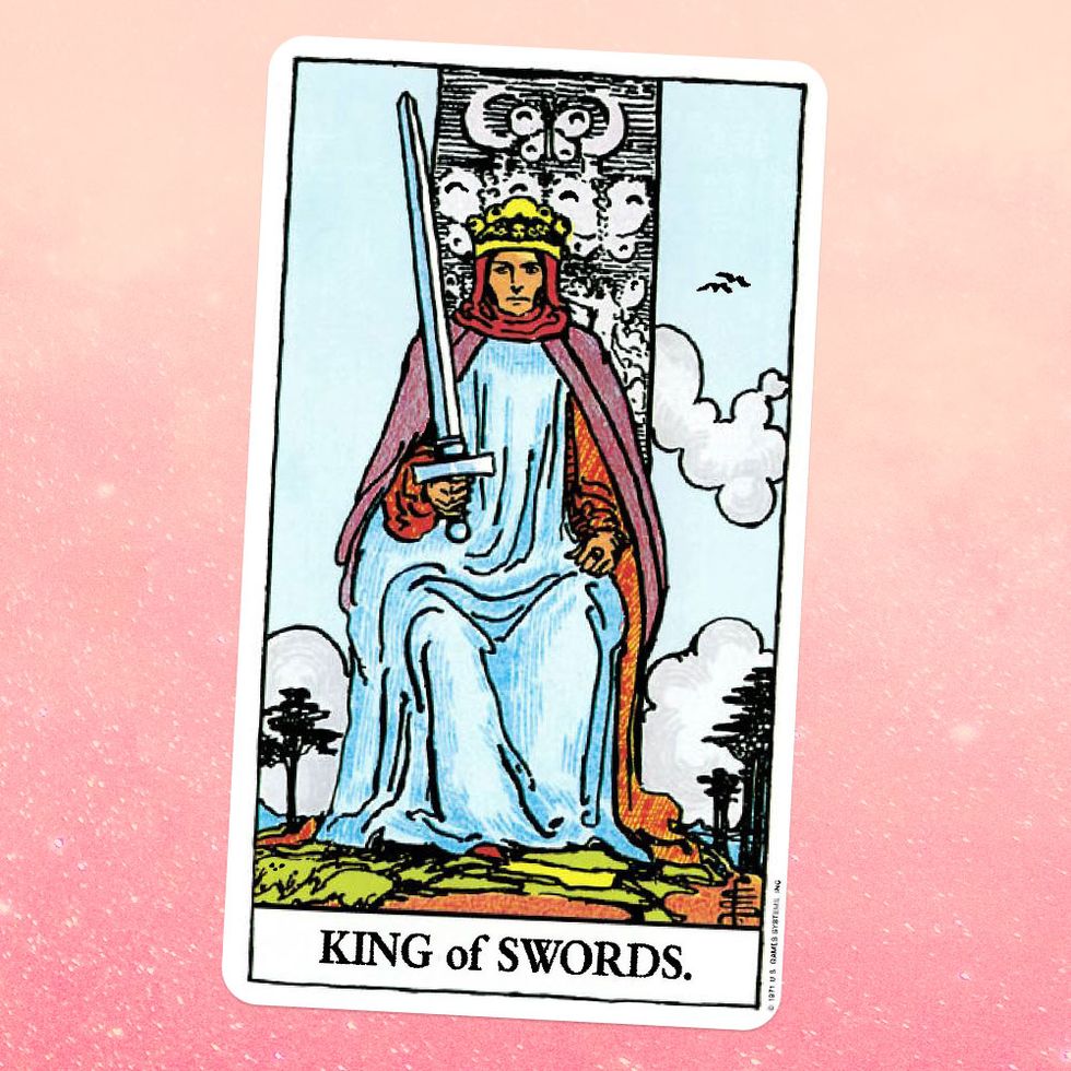 the tarot card the king of swords, showing a white man in a white robe, purple cape, and gold crown sitting on a throne while holding a sword