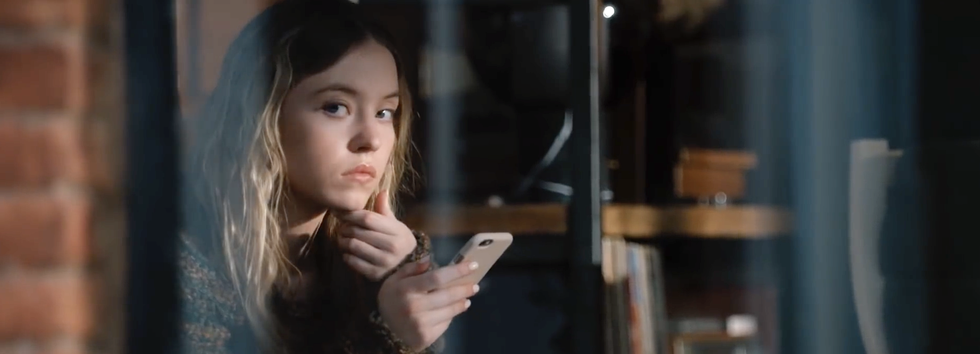 sydney sweeney in the voyeurs, holding phone and looking out the window