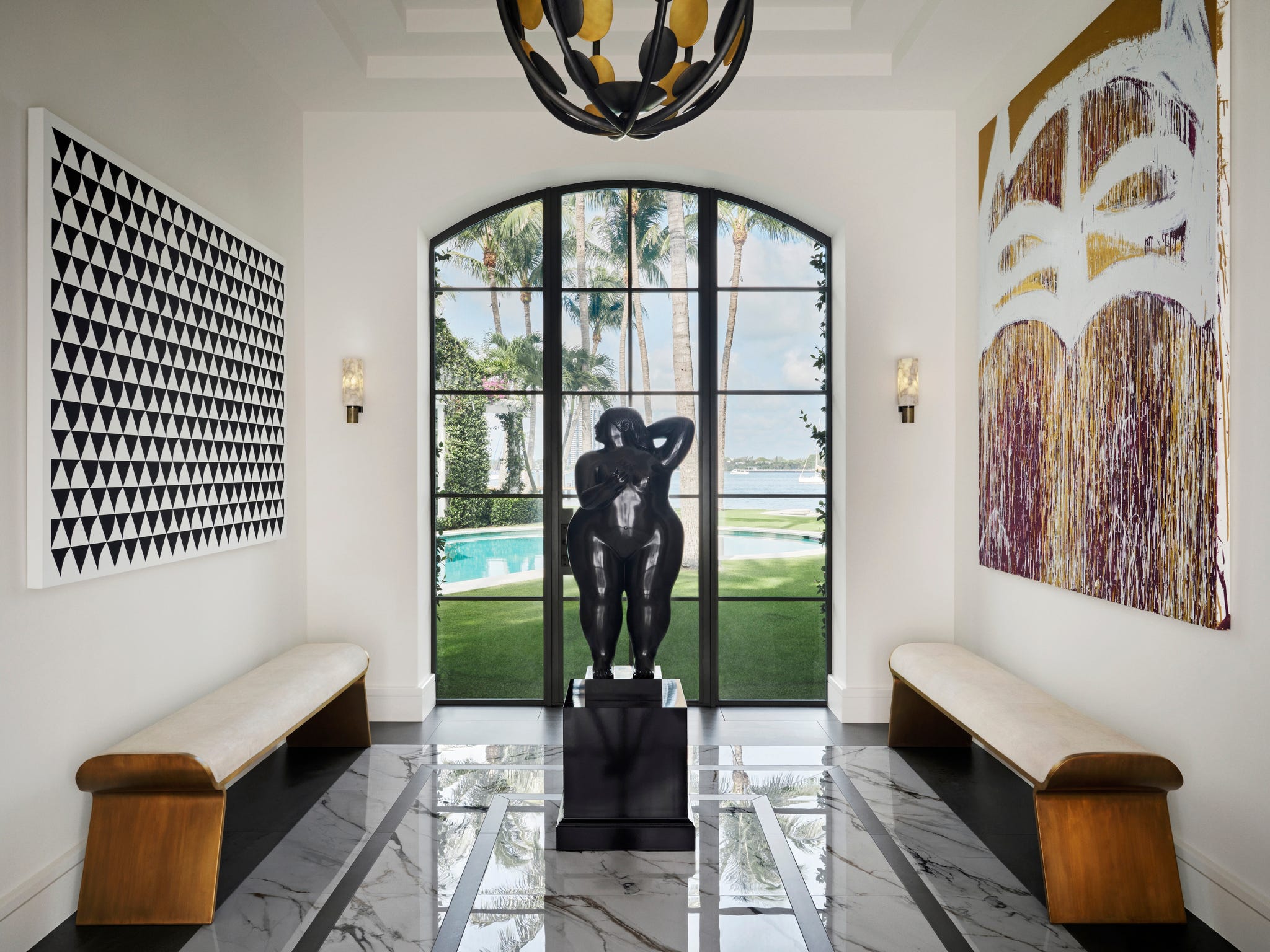 entry with art on either wall and a sculpture and doors overlooking a pool