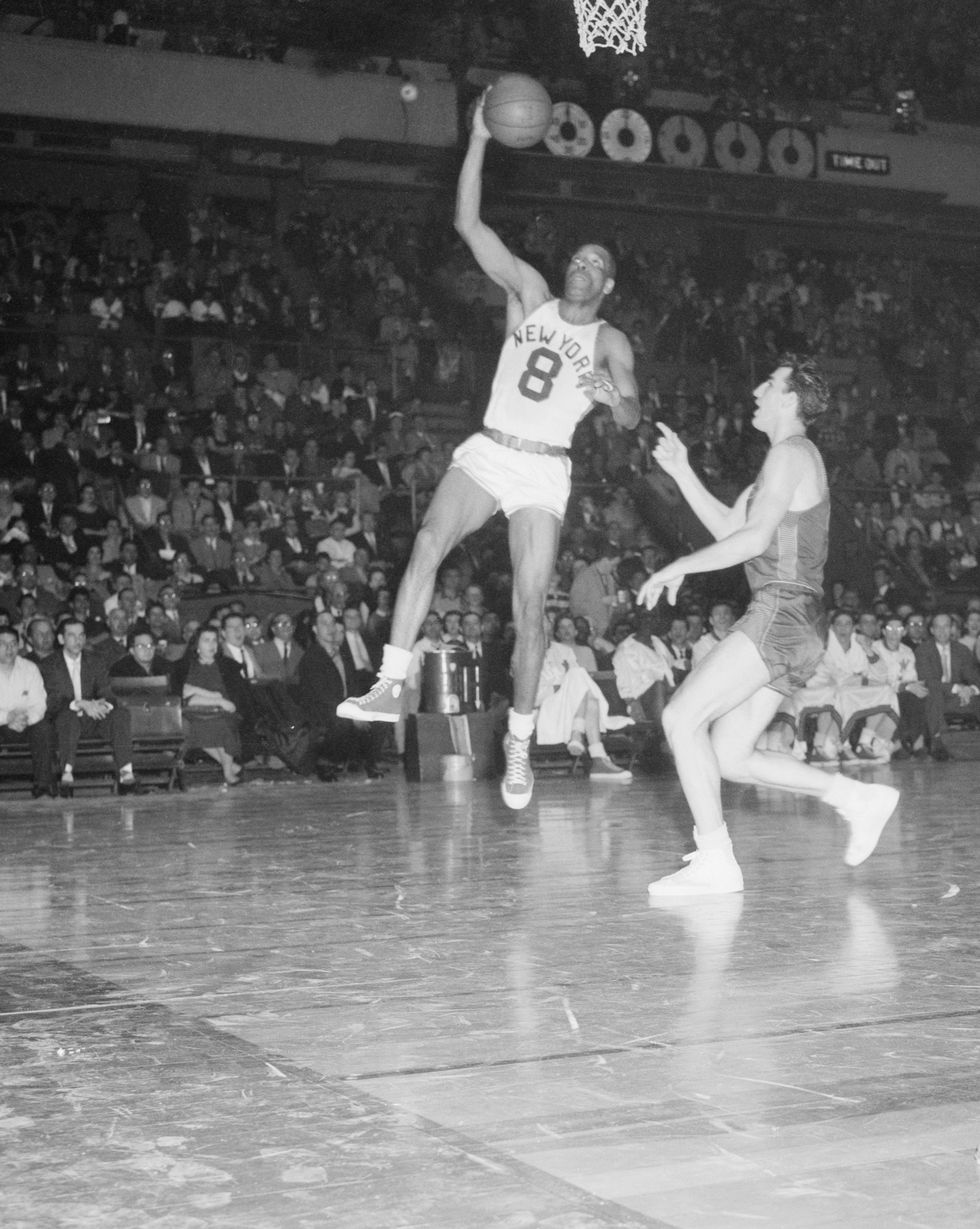 a black and white photo of sweetwater clifton jumping up to dunk the ball in madison square garden as another player points at him
