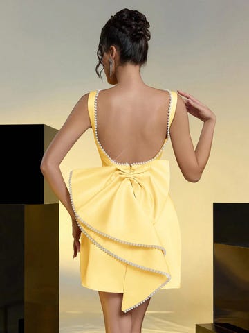 back view of a model in a stylish yellow dress with a decorative bow and pearl detailing