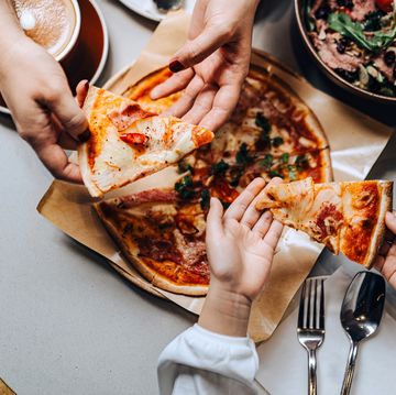 table top view of mother and daughter enjoying lunch together, they are sharing a freshly made pizza along with a bowl of salad in cafe. family enjoying a joyful and tasty lunch. family bonding and eating out. people, food and lifestyle