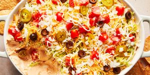 layered dip with sour cream, shredded lettuce, shredded cheese, black olives, tomatoes and jalapenos