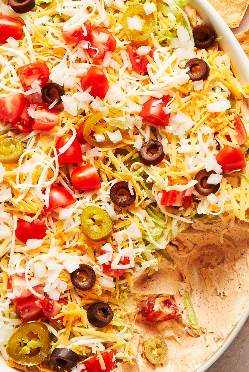 layered dip with sour cream, shredded lettuce, shredded cheese, black olives, tomatoes and jalapenos