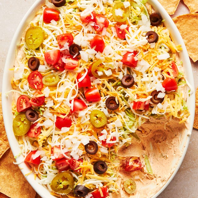 layered dip with sour cream, shredded lettuce, shredded cheese, black olives, tomatoes and jalapenos