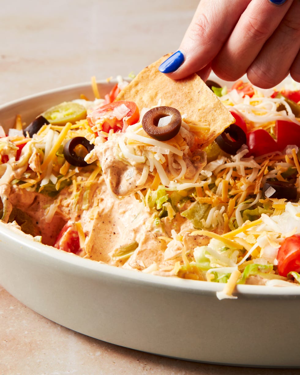 layered dip with sour cream, shredded lettuce, shredded cheese, black olives, tomatoes and jalapenos