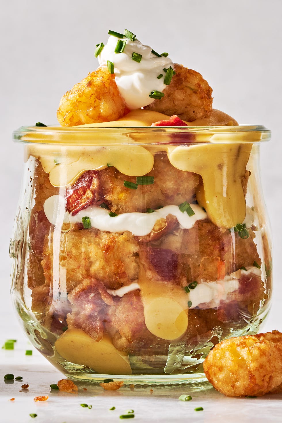 tater tots in a mason jar layered with sour cream, cheese, bacon, and chives