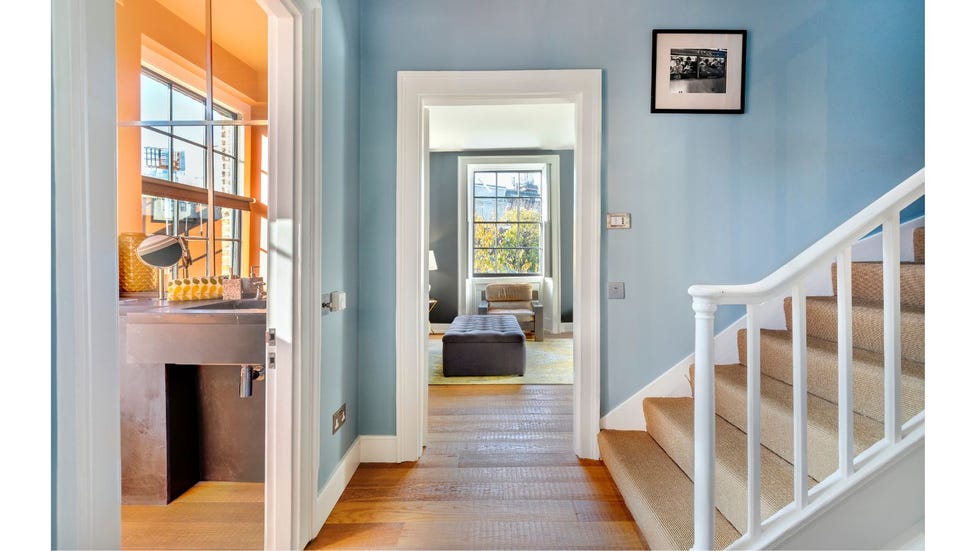 light blue landing with wooden floor leads to an orange bathroom and living room