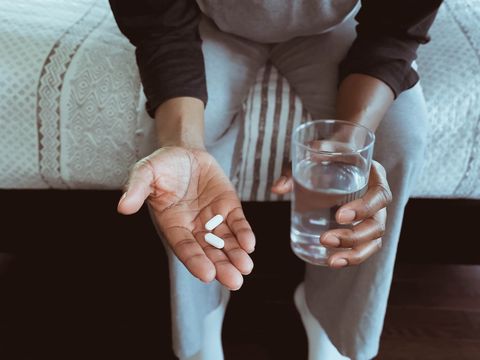 close up of woman sitting on edge of bed holding pills and glass of water