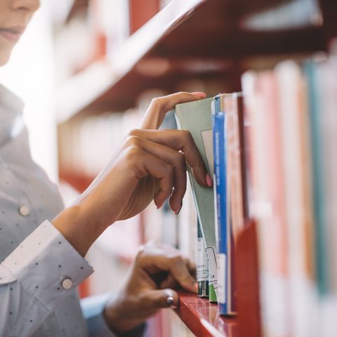 woman taking book out from library shelf
