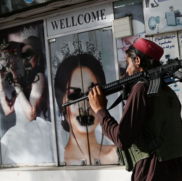 taliban fighter walks by a graffitied photo of woman