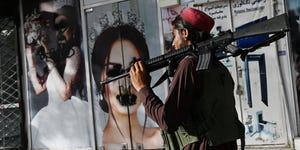 taliban fighter walks by a graffitied photo of woman