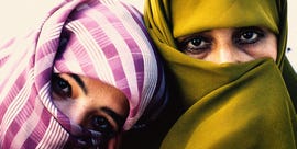 two afghan women in head scarves covering all of their faces besides their sad looking eyes