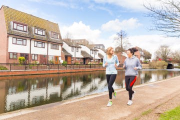 two individuals jogging along a canal in a residential area