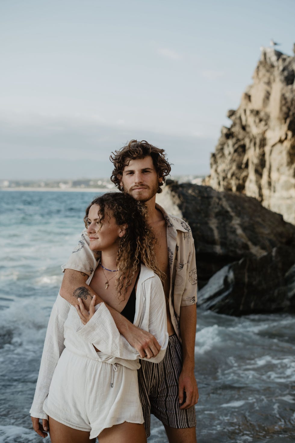 a couple embracing on a beach near rocky terrain