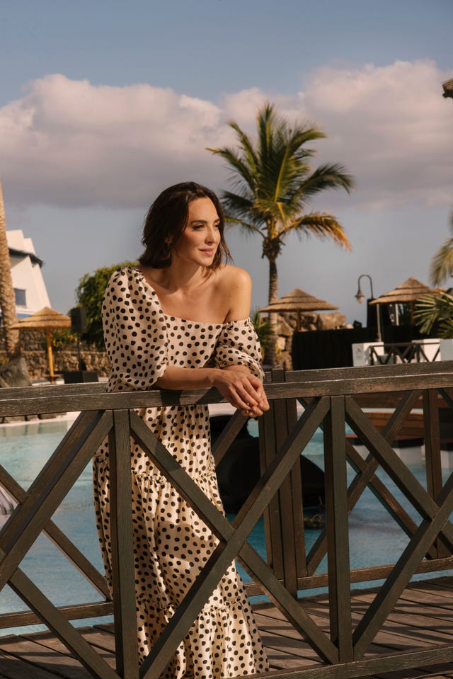 Tamara Falcó con un vestido asimétrico color crema con estampado en lunares, se apoya en la barandilla de la piscina de un resort.