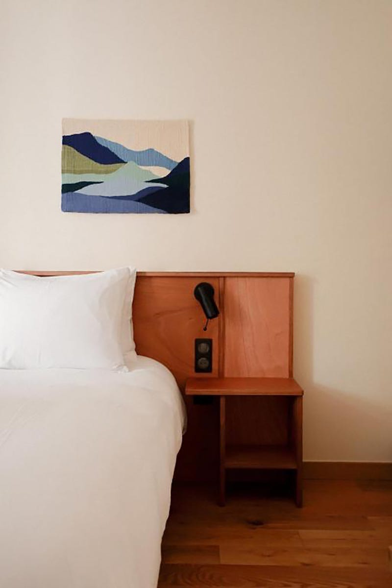 dormitorio con tapiz en azules, cabecero de madera y colcha blanca