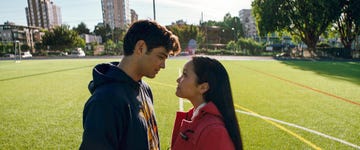 two individuals are positioned closely facing each other on a green soccer field surrounded by buildings and trees